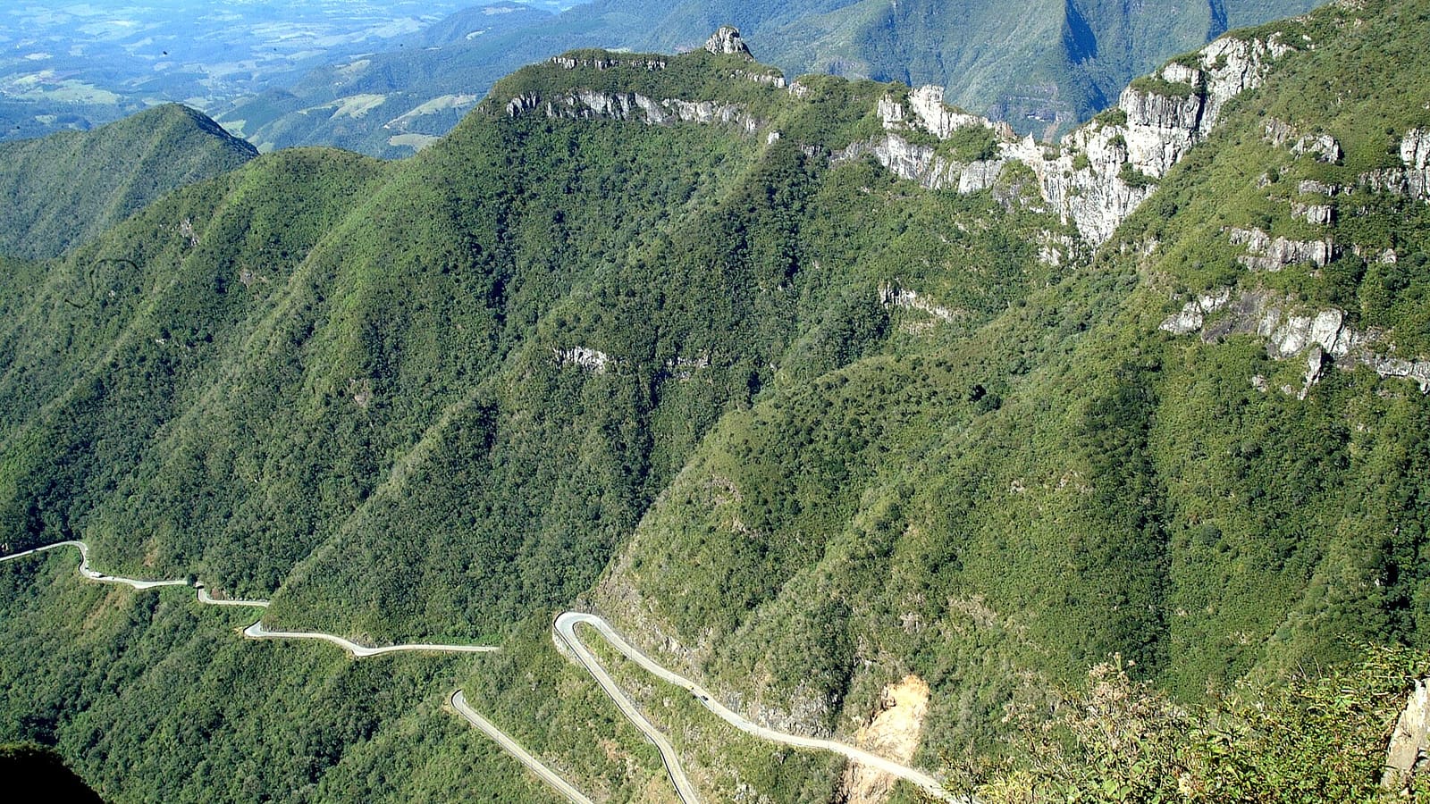 Vista do alto da Serra do Rio do Rastro, em Santa Catarina, com a estrada em curvas fechadas descendo entre paredões de mata